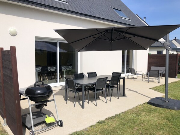 An outdoor patio with a table and chairs, a grill, and a large umbrella.