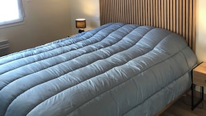 A bedroom with a bed, a nightstand, a lamp, a window, and a wooden slat wall. - Pretty house with enclosed garden close to amenities in ERDEVEN. (Erdeven)