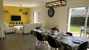 A dining area with a table set for four, a sofa, a TV, and a window with a view of the outdoors. - Pretty house with enclosed garden close to amenities in ERDEVEN. (Erdeven)