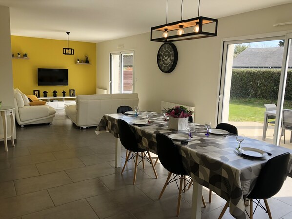 A dining area with a table set for four, a sofa, a TV, and a window with a view of the outdoors.