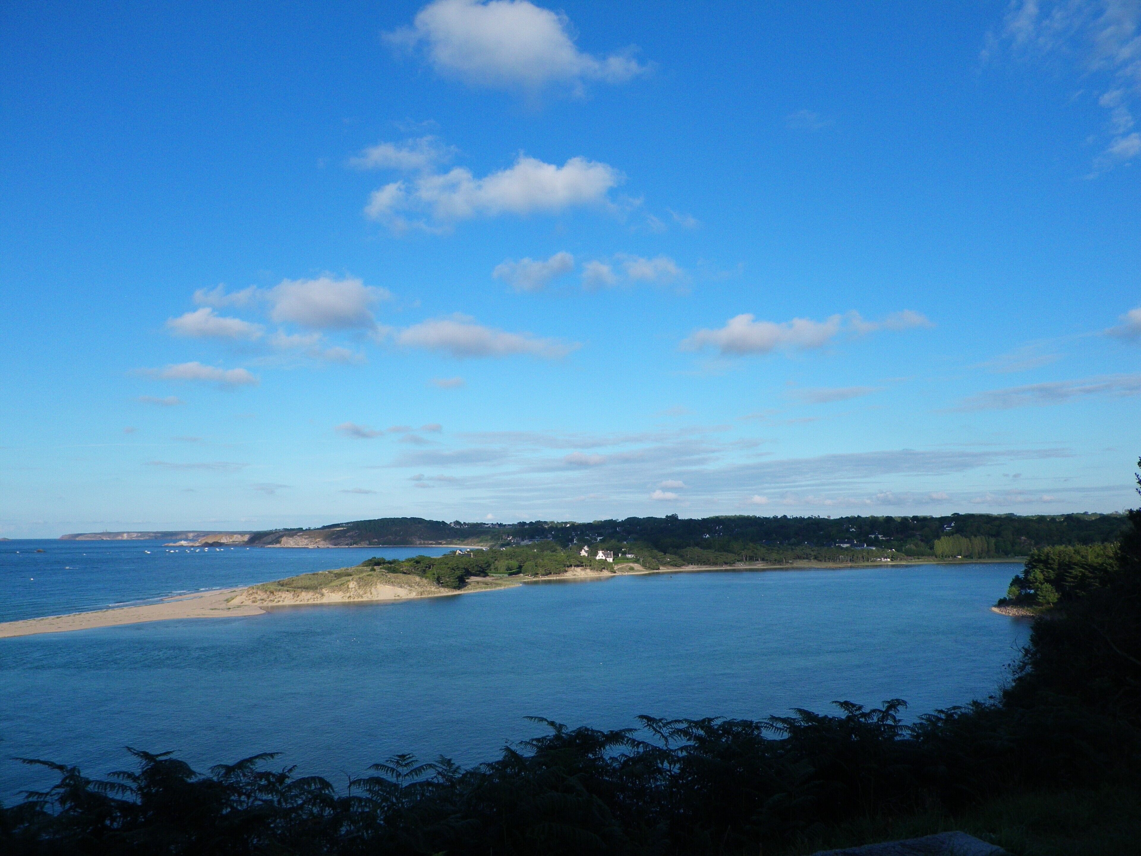 A coastal landscape with a clear sky, a sandy beach, and a calm sea.