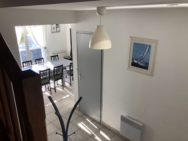 Un comedor con una mesa, sillas, una lámpara colgante blanca, un radiador y un cuadro en la pared.