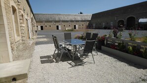 An outdoor patio with a table and chairs, surrounded by stone walls and a gravel ground. - OMAHA BEACH COTTAGE BETWEEN EARTH AND SEA (Formigny)