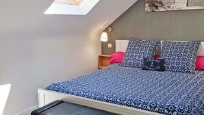 A bedroom with a skylight, a bed with patterned bedding, a bench, and a nightstand with a lamp. - Bright duplex apartment in Belle Ile en Mer  (Le Palais)