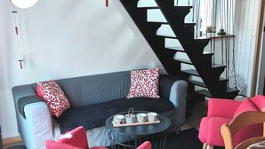 A modern living room with a staircase, wooden beams, a sofa, red chairs, and a small table with cups. - Bright duplex apartment in Belle Ile en Mer  (Le Palais)