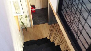 A staircase with wooden steps and a black handrail, leading to a room with a white door and a red bucket on the floor. - Bright duplex apartment in Belle Ile en Mer  (Le Palais)