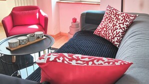 A cozy living room with a grey sofa, red and white patterned pillows, a red armchair, and a small round table with decorative items. - Bright duplex apartment in Belle Ile en Mer  (Le Palais)
