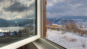 A view through a window of a snowy landscape with mountains, a lake, and a small village. - Cottage with magnificent view of the Lake in Gérardmer, 8 people (Gérardmer)