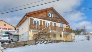 A two-story house with a wooden balcony, a car parked in front, and a snow-covered ground. - Cottage with magnificent view of the Lake in Gérardmer, 8 people (Gérardmer)