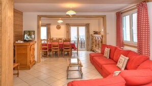 A living room with a red sofa, wooden furniture, a glass coffee table, and a dining area with a red tablecloth. - Cottage with magnificent view of the Lake in Gérardmer, 8 people (Gérardmer)