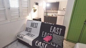 Um espaço de estar pequeno e aconchegante com um sofá de design preto e branco. Uma porta verde é visível ao fundo.
