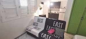 Un petit espace de vie compact, avec un canapé au motif noir et blanc et orné de motifs textuels. Une porte verte est visible à l’arrière-plan.