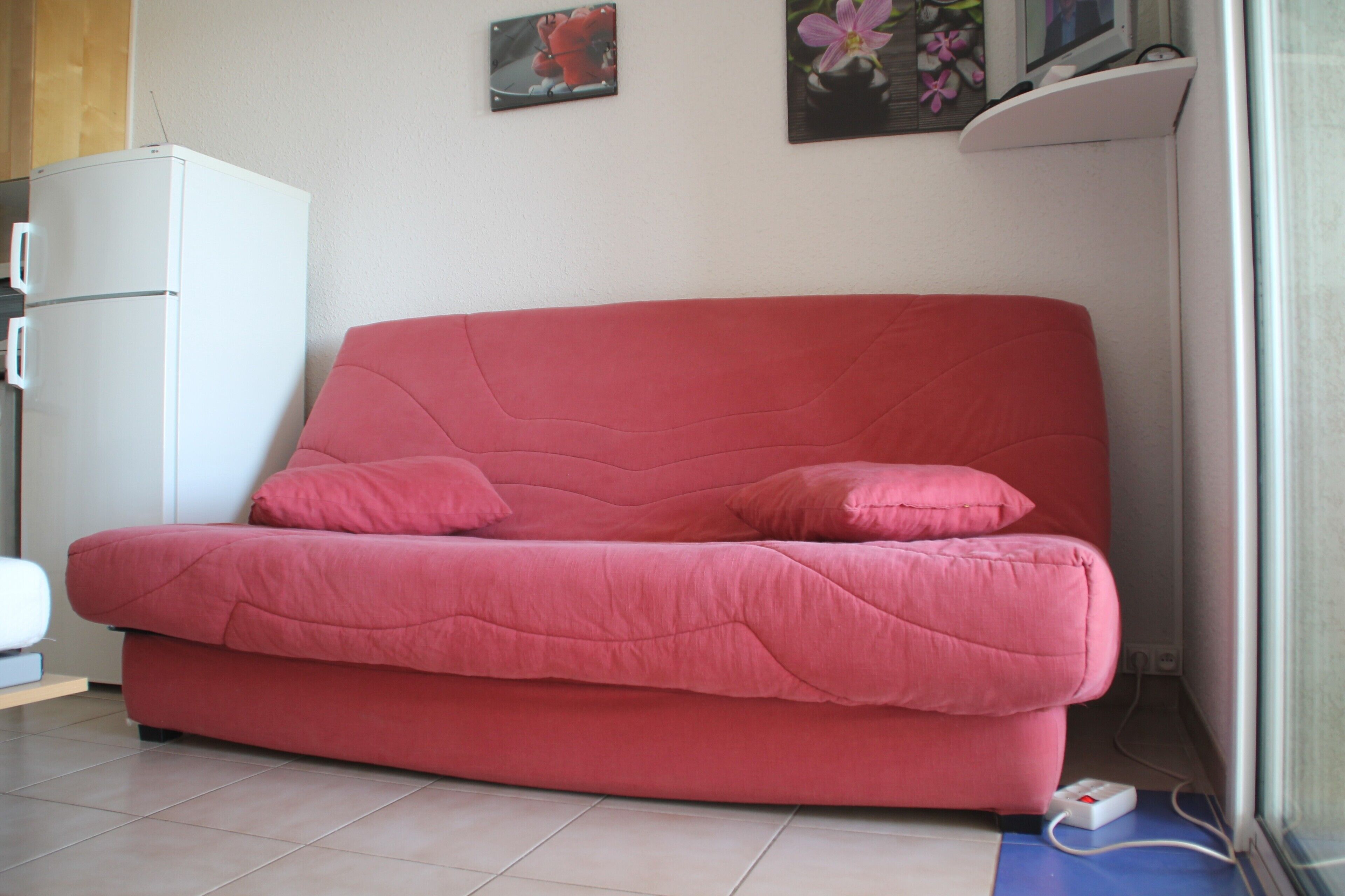 A red sofa in a room with a white cabinet and a picture on the wall.