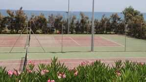 Tenniskenttä, jossa on verkko, ja jota ympäröivät puut. Kentältä on näkymä merelle.