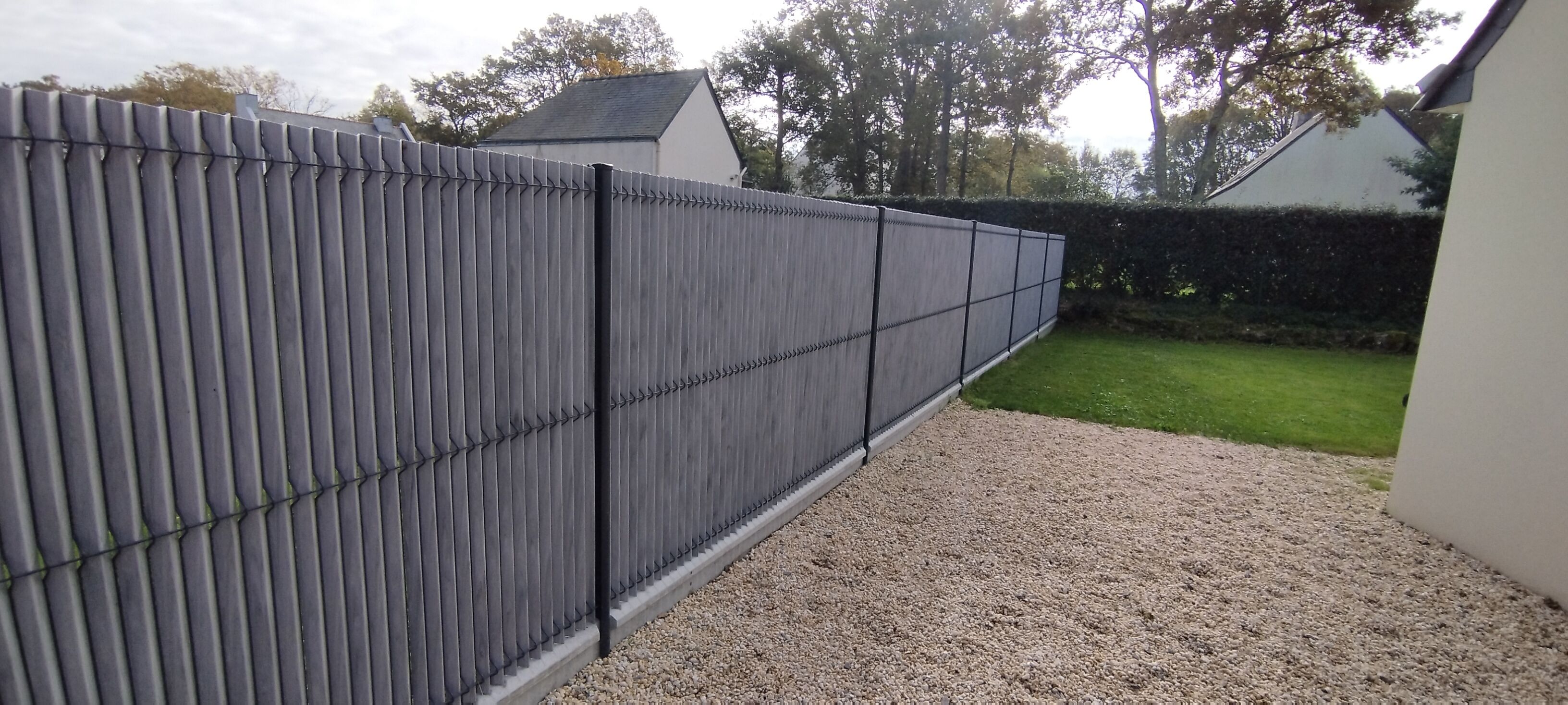 A grey metal fence with vertical bars, a gravel path, and a green lawn.