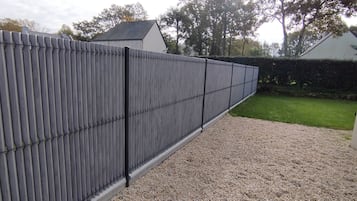 A grey metal fence with vertical bars, a gravel path, and a green lawn.