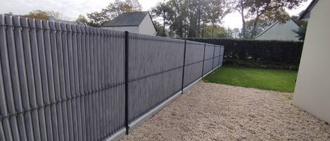 A grey metal fence with vertical bars, a gravel path, and a green lawn.