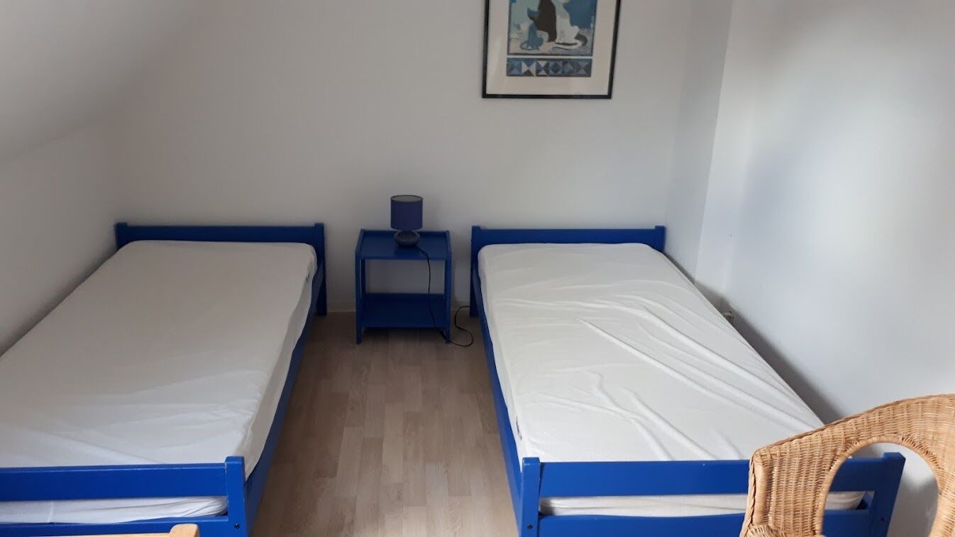 Ein kleines Hotelzimmer mit zwei Einzelbetten, einem Nachttisch mit Lampe und einem gerahmten Bild an der Wand.