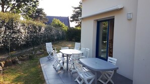 Terrassa exterior amb taula i caires, una porta de vidre i una paret blanca.