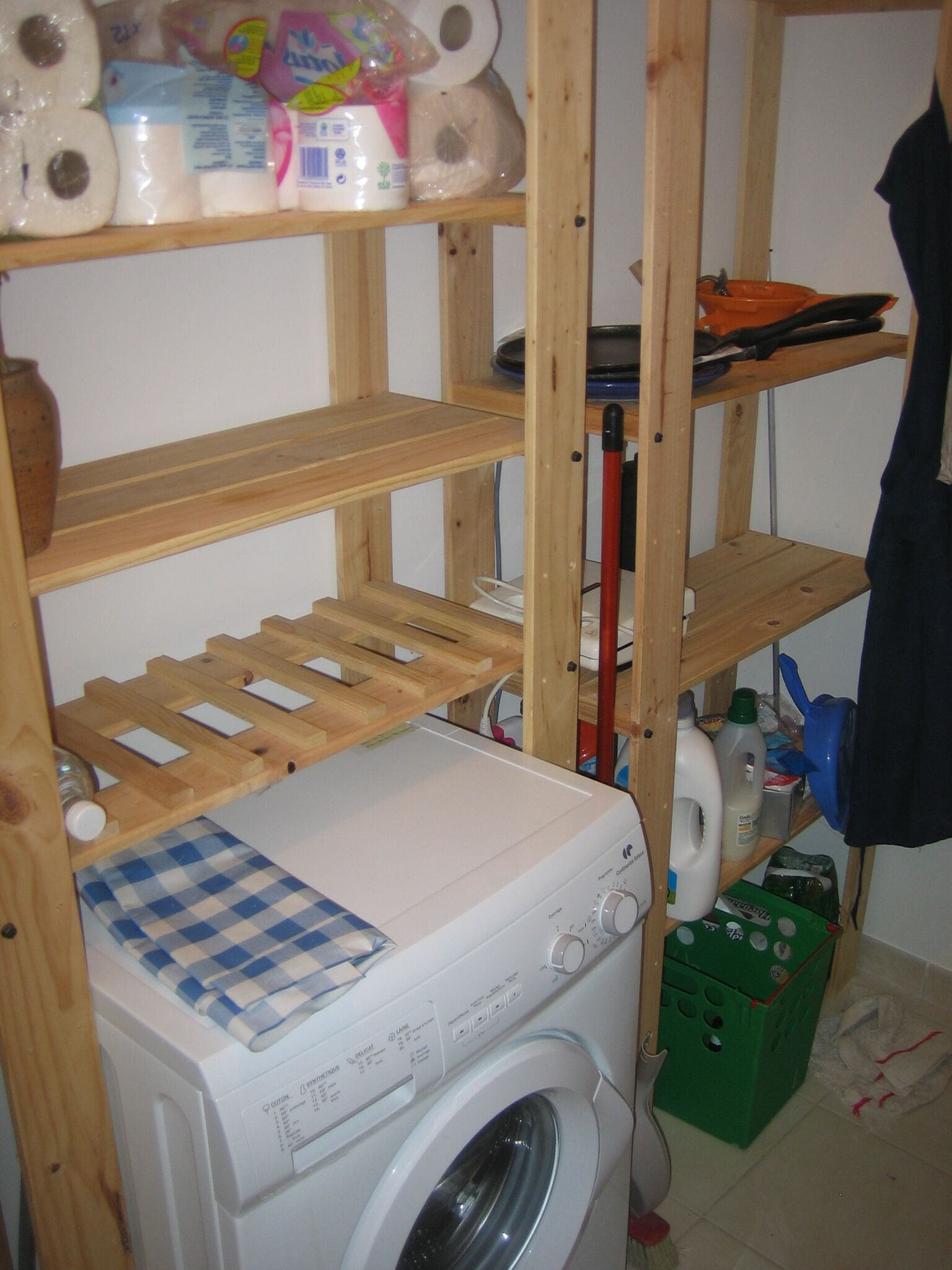 A laundry area with a washing machine, shelves with toiletries, and a drying rack.