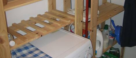 A laundry area with a washing machine, shelves with toiletries, and a drying rack.