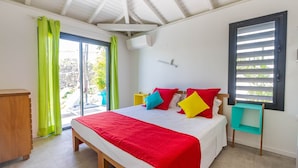 A bedroom with a bed, a wooden nightstand, a green chair, and a window with blinds. - Villa Passion 4 people, sea view, in the heart of the Riviera of the islands of Guadeloupe (Sainte Anne)