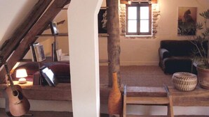 A cozy loft-style room with exposed wooden beams, a stone wall, a fireplace, a couch, and a guitar.