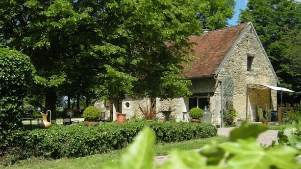 A stone building with a sloped roof, surrounded by lush greenery and trees.