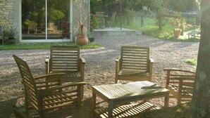 An outdoor seating area with wooden chairs and a table, surrounded by a gravel path and greenery.