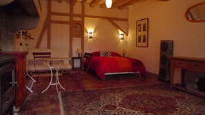 A bedroom with a bed, a chair, a table, and a fireplace.