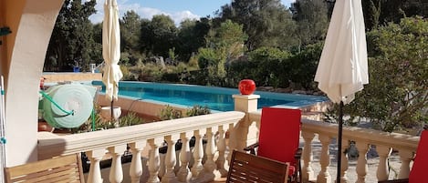 Een balkon met een zwembad, rode stoelen en een tafel.