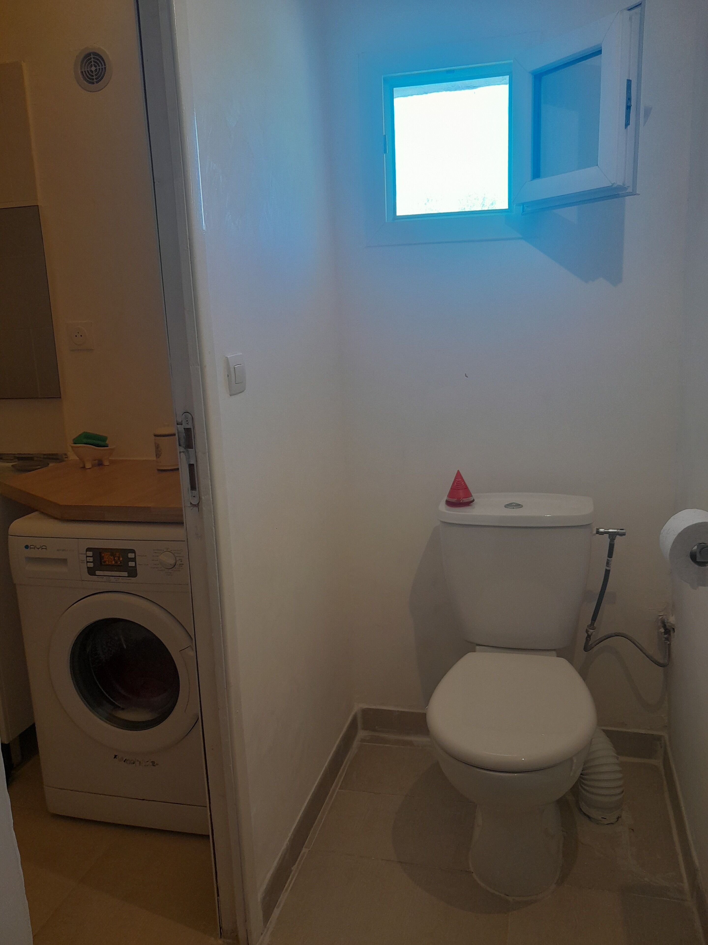 Une petite salle de bain avec des toilettes, un lave-linge et une fenêtre.