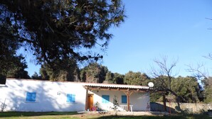 A white building with blue shutters, a wooden porch, and a garden area. - 70 m2 Rental near sea / mountain (Cargèse)