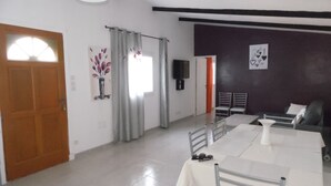 A dining area with a table and chairs, a wooden door, a window with curtains, and a wall-mounted TV. - 70 m2 Rental near sea / mountain (Cargèse)