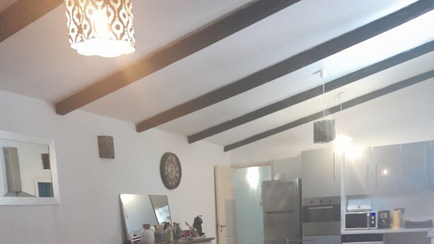 A modern living room with a sofa, a wooden coffee table, and a dining area with chairs and a table. There is a kitchen in the background with appliances and cabinets. - 70 m2 Rental near sea / mountain (Cargèse)