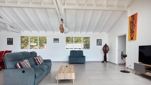 A spacious living room with a blue sofa, a wooden coffee table, and a TV stand. - Villa Colibri in Deshaies (Deshaies)