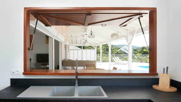 A kitchen with a large window, a sink, and a wooden cutting board with knives. - Villa Colibri in Deshaies (Deshaies)