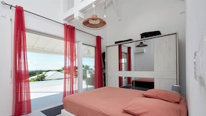 A modern bedroom with a large bed, red curtains, a ceiling fan, and a view of the outdoors. - Villa Colibri in Deshaies (Deshaies)
