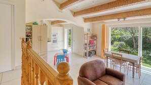 Een ruime woonkamer met een hoge nok, houten balken, een eettafel met stoelen, een bank en een keuken op de achtergrond.