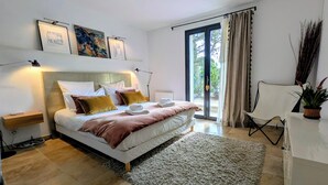 A modern bedroom with a large bed, bedside tables, a desk, a chair, and a view through a glass door. - Villa, private heated pool, beautiful view of the Alpilles (Eygalières)