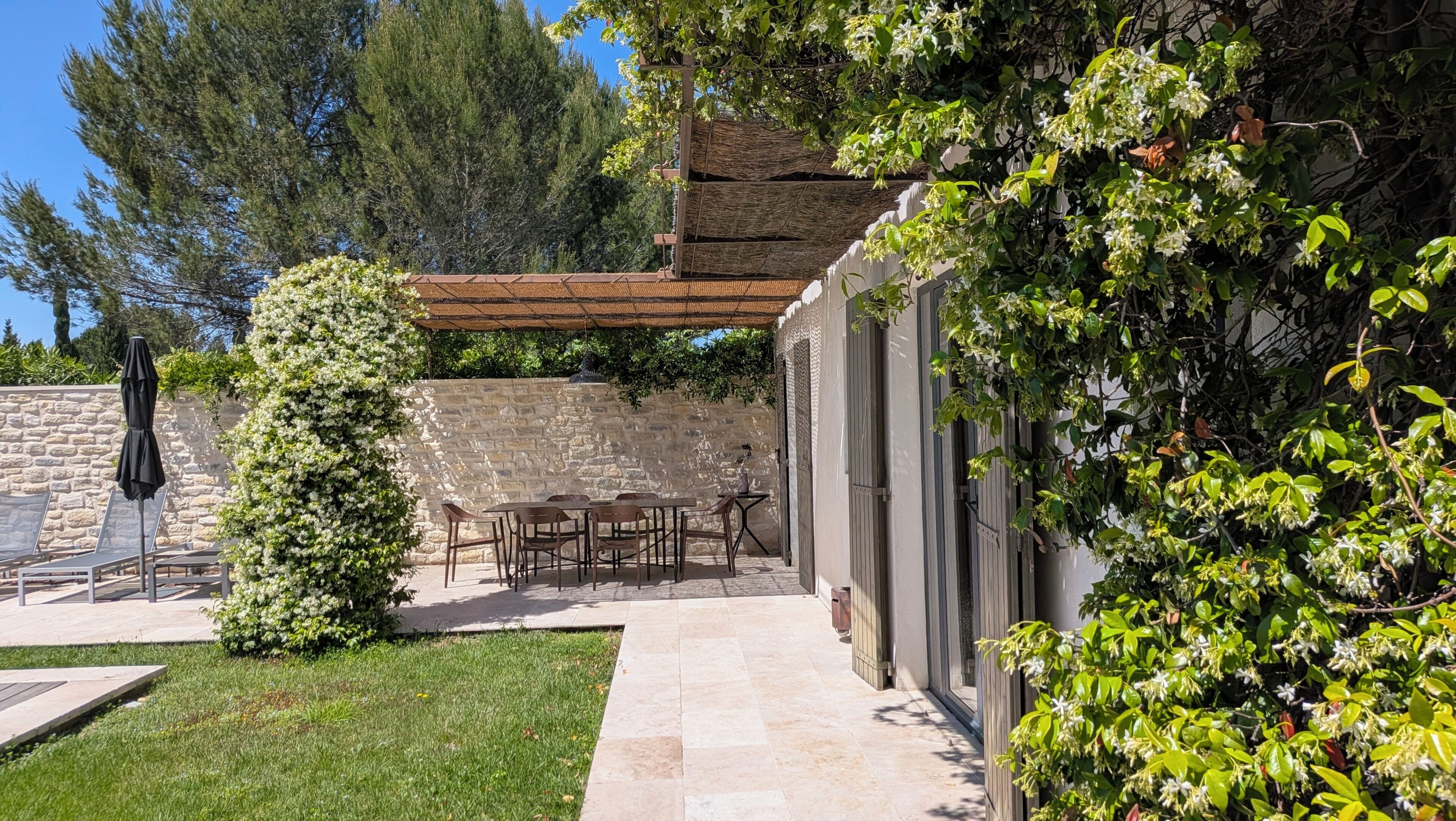 Une terrasse extérieure avec des murs en pierre, une pergola et une table entourée de chaises.