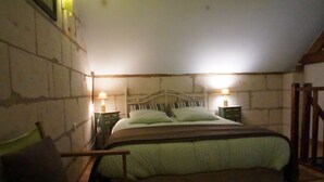 A bedroom with a bed, two bedside tables, a chair, and a wooden ladder. - For a stay in 2 very quiet in a tufa house in Anjou (Gennes-Val De Loire)