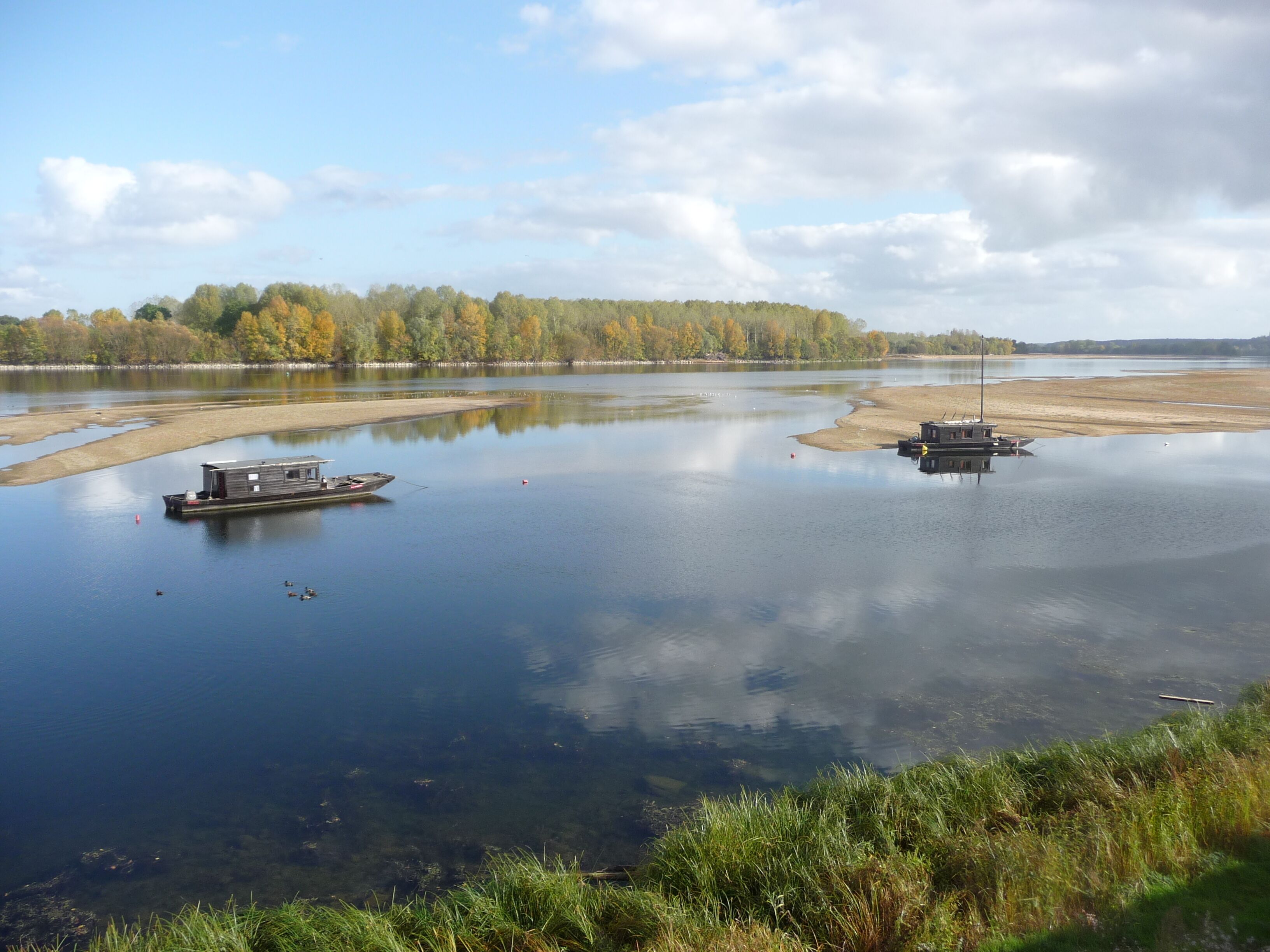 Une rivière paisible, avec des bateaux et des rives bordées d’arbres.