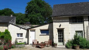 A stone building with a white door, a window, and a small porch with a table and chairs. - For a stay in 2 very quiet in a tufa house in Anjou (Gennes-Val De Loire)