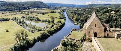 Un edificio histórico con un río en primer plano y un paisaje montañoso al fondo.
