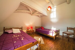 Une chambre avec deux lits, des meubles en bois, une petite table avec une lampe et une fenêtre laissant entrer la lumière naturelle.