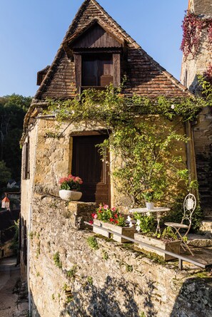 Ein rustikales Steinhaus mit einer Holztür, einem kleinen Balkon mit Topfpflanzen und einer Steinsäule.