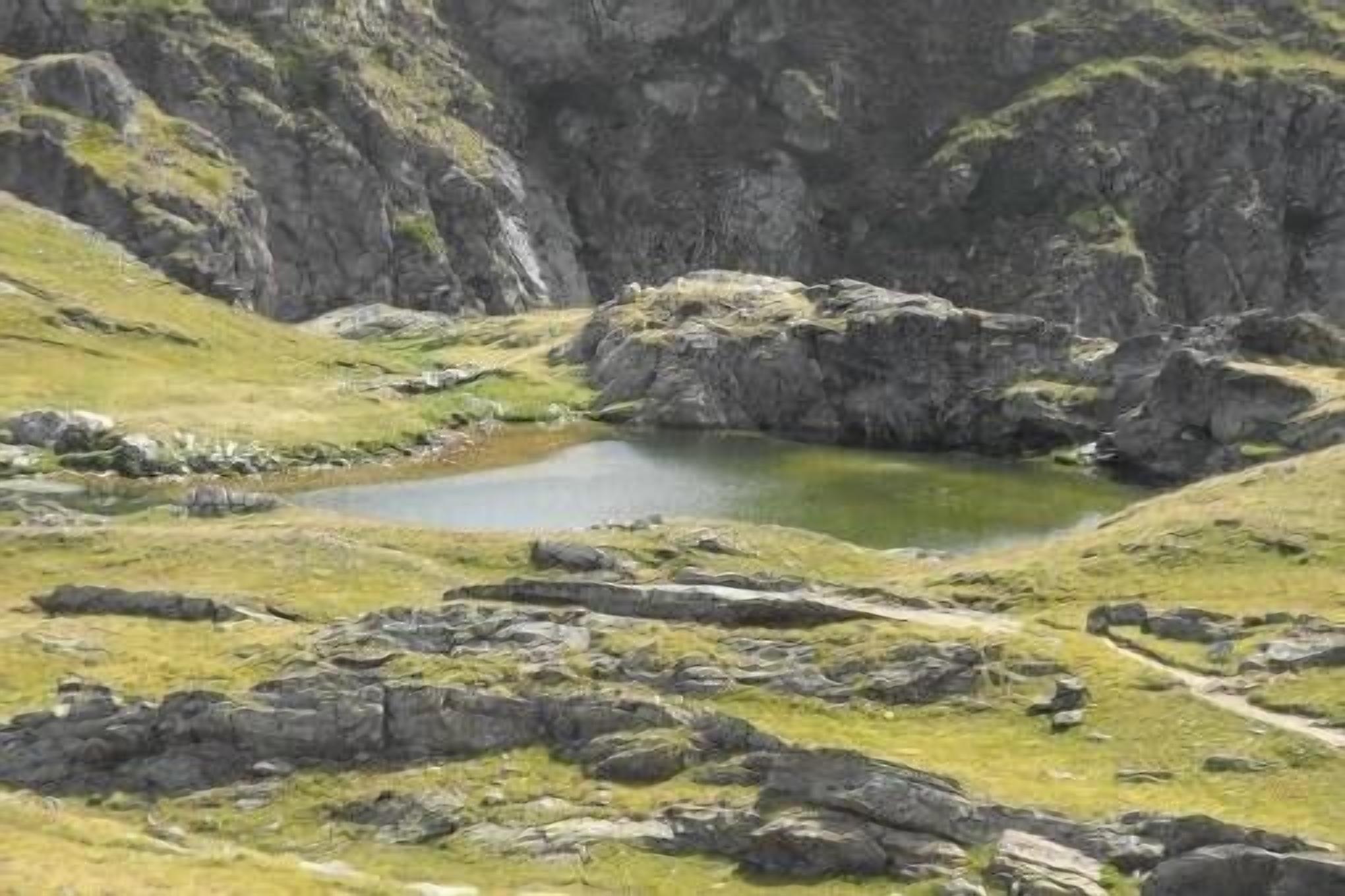 A rocky landscape with a small pond and a dirt path.