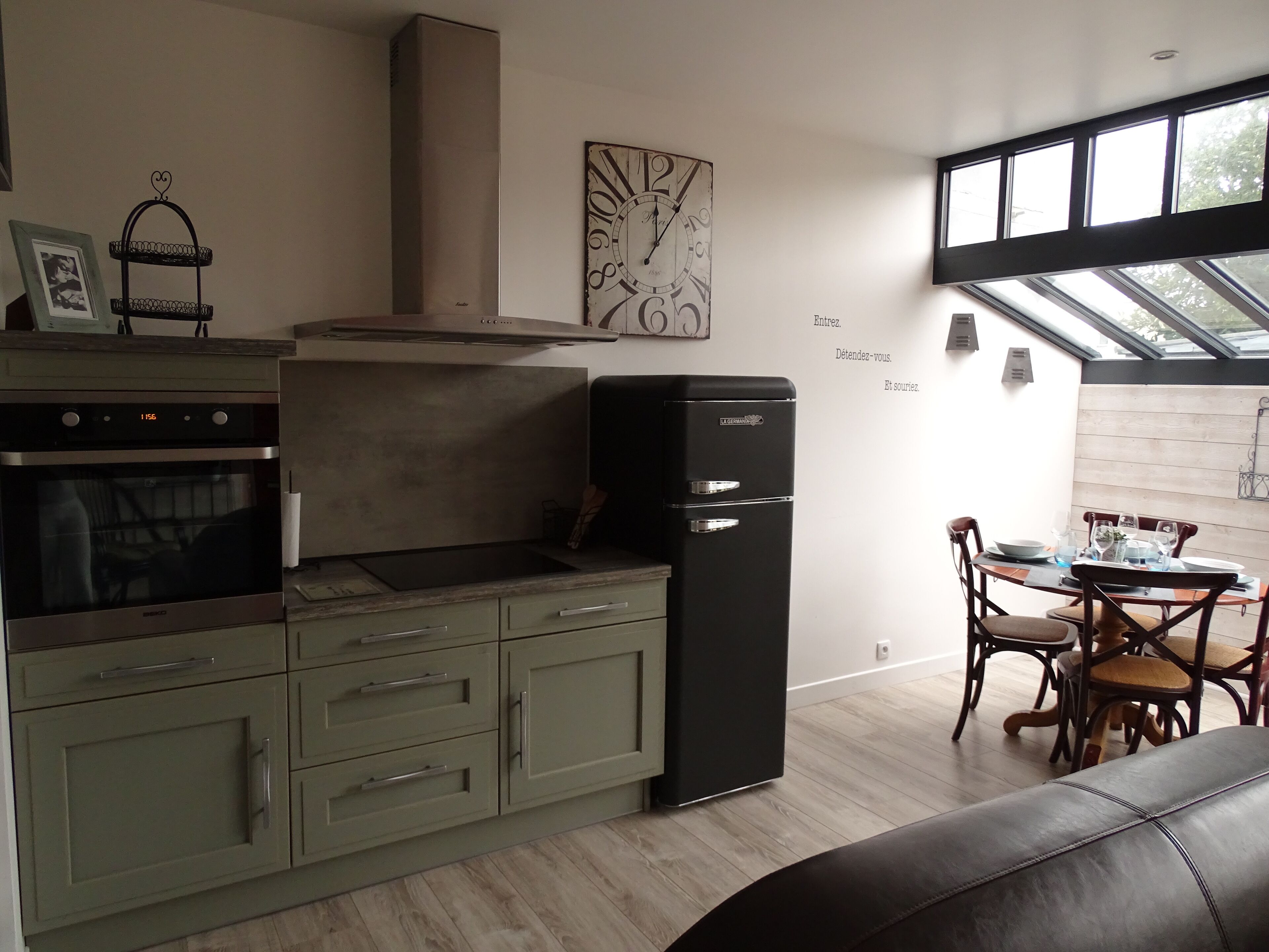 A modern kitchen with a built-in oven, a black refrigerator, and a dining area with a table set for two.
