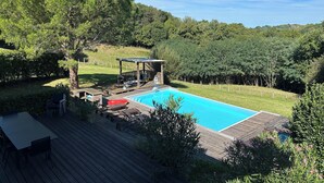 A backyard with a swimming pool, wooden deck, and a covered seating area with chairs and a table. - Basque farmhouse with swimming pool (Mouguerre)
